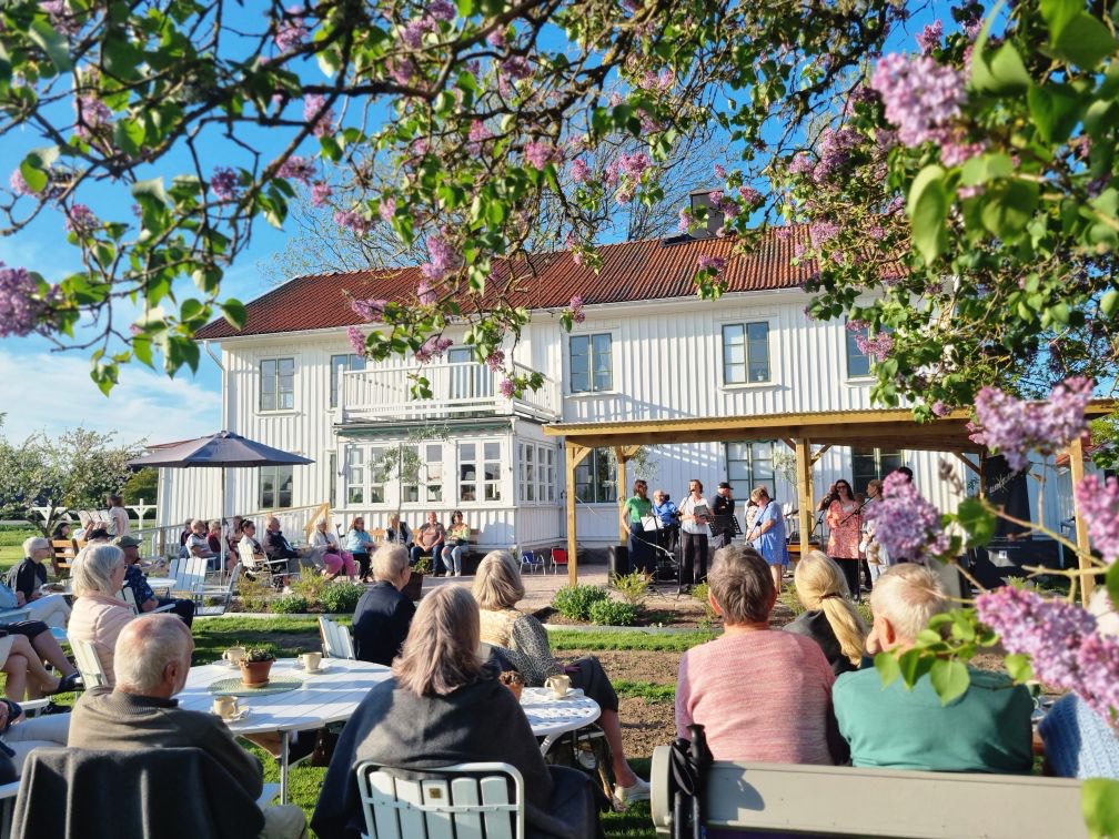 Folk samlade framför en vit prästgård tidigt på våren.
